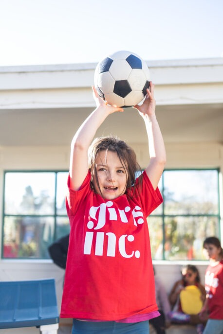 Young girl holding a soccer ball above her head